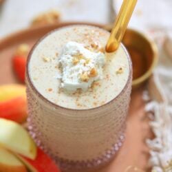 glass with beige smoothie, gold straw, and apples
