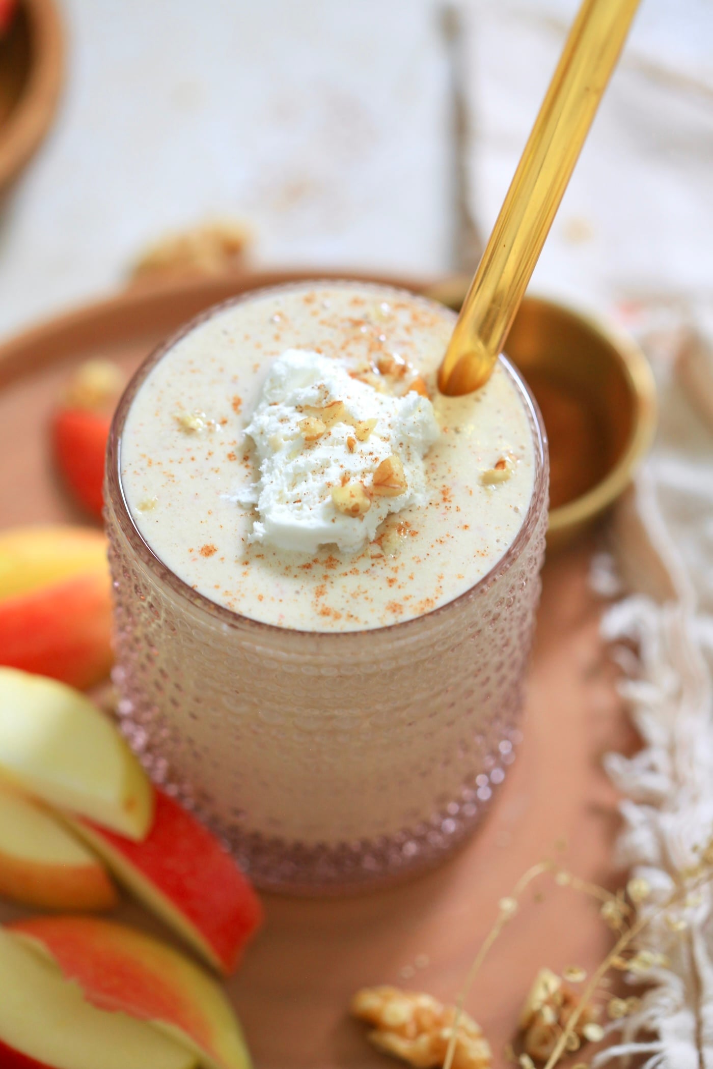 glass with beige smoothie, gold straw, and apples