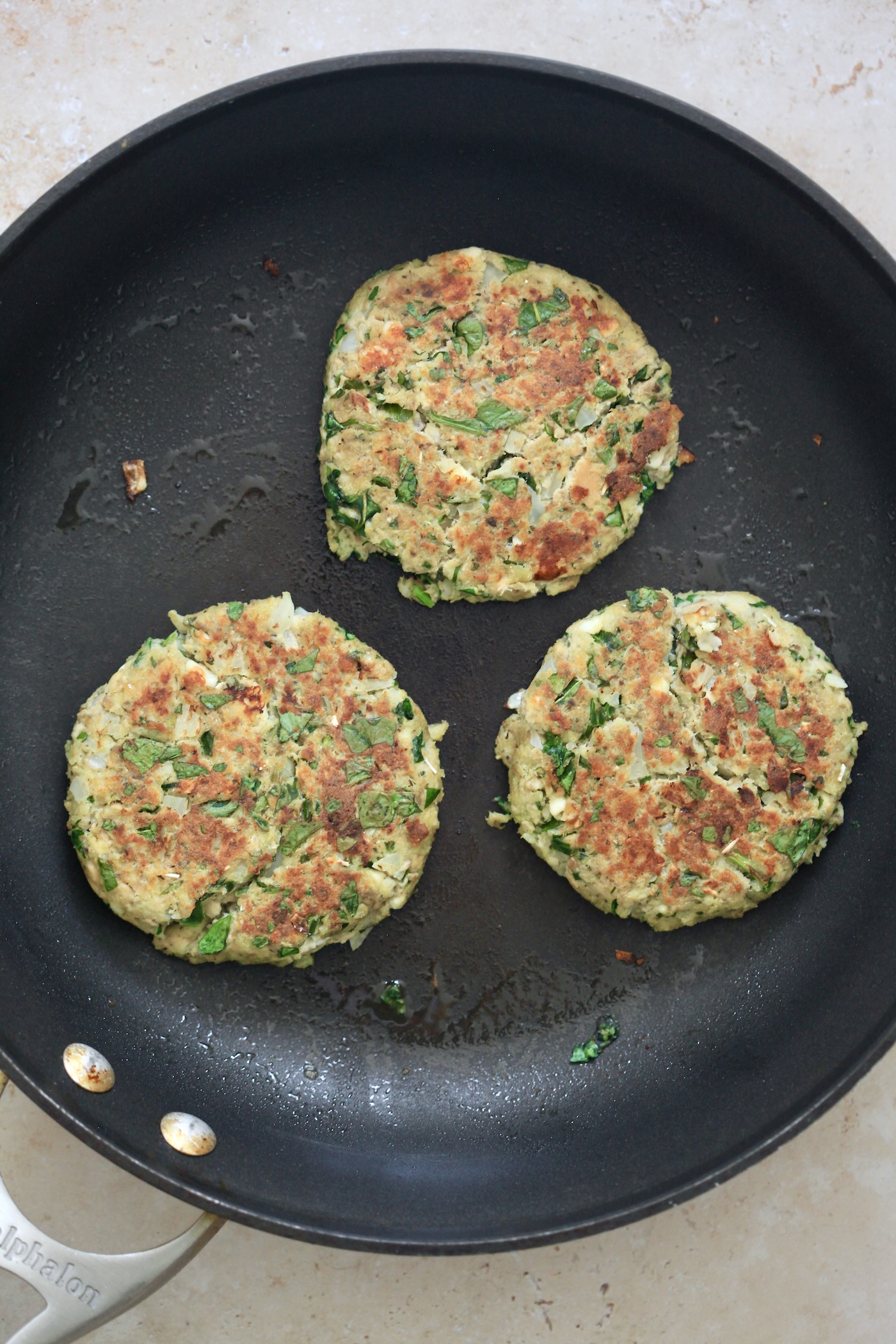 three salmon burgers cooking on black pan.