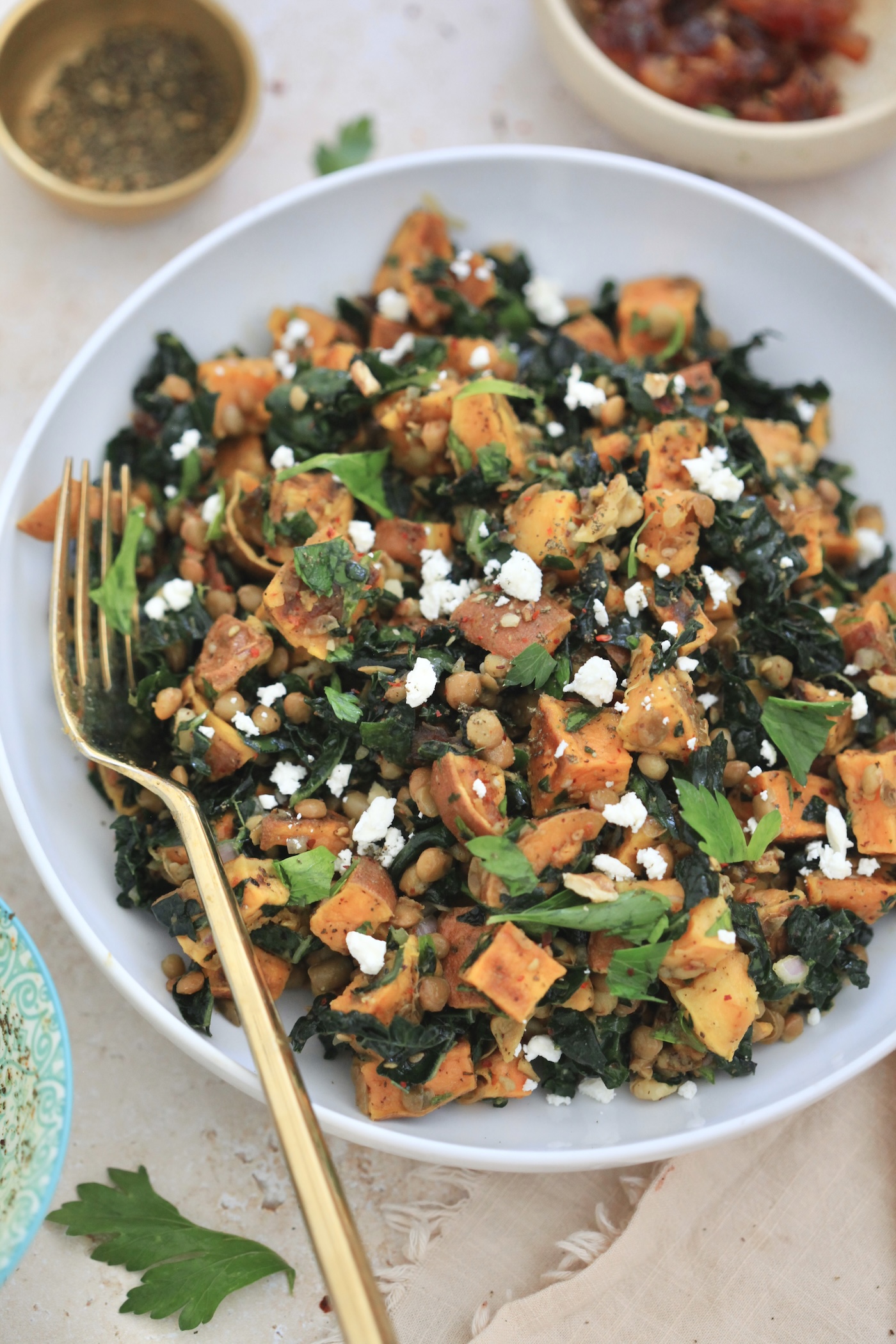 white bowl with sweet potatoes, kale and gold fork