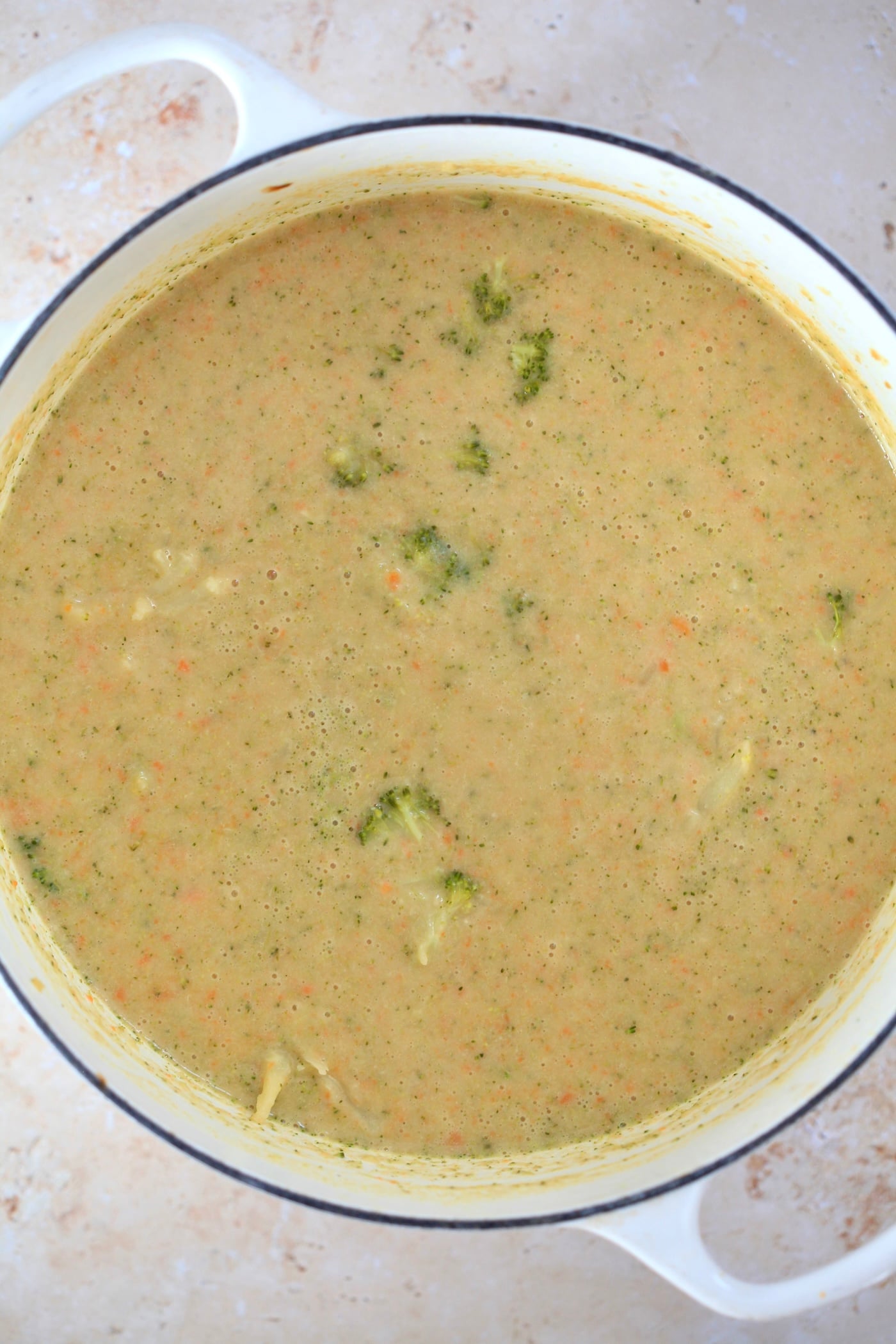 mostly blended yellow soup in white pot with broccoli.