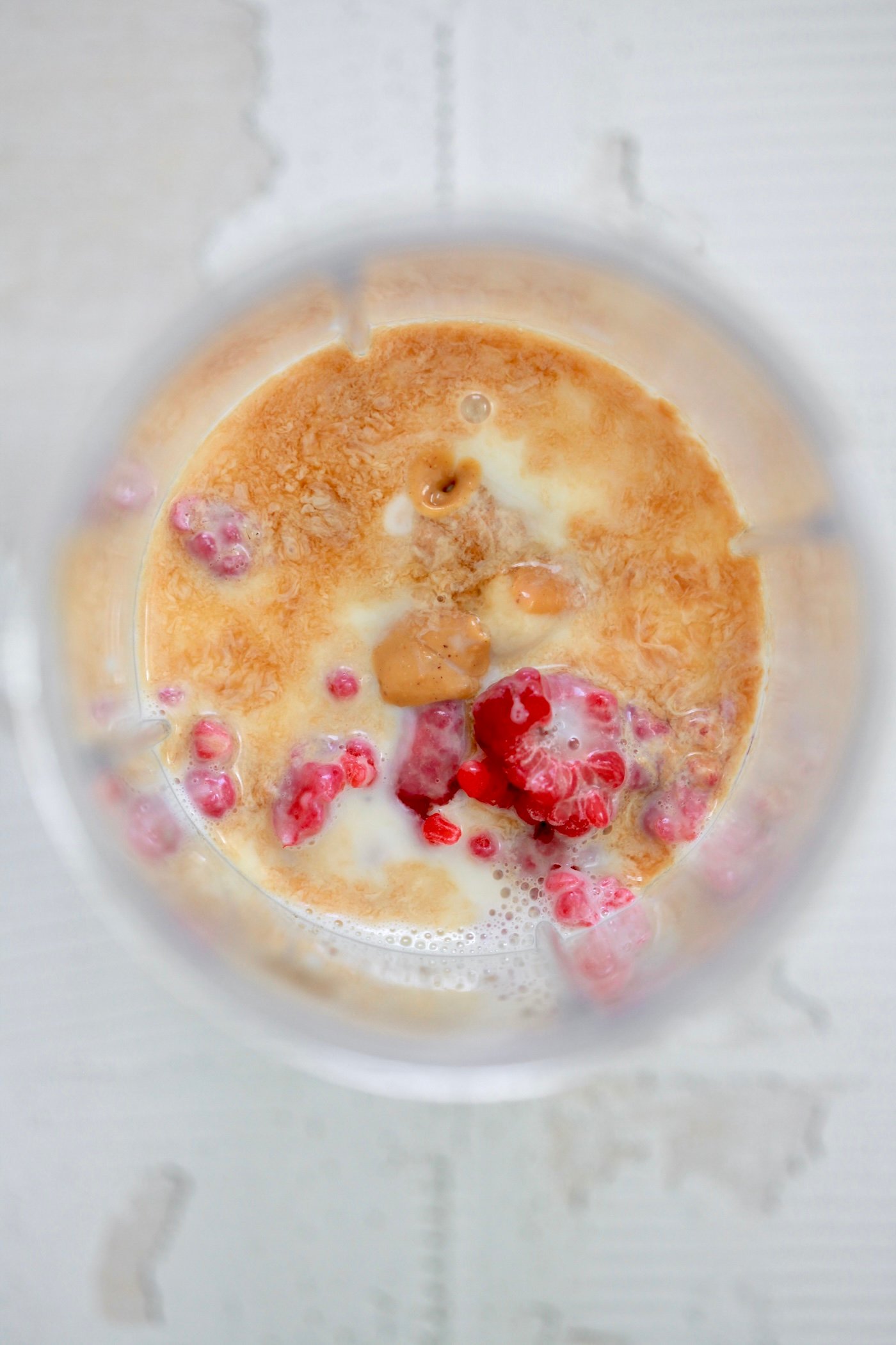 milk in blender jar with raspberries