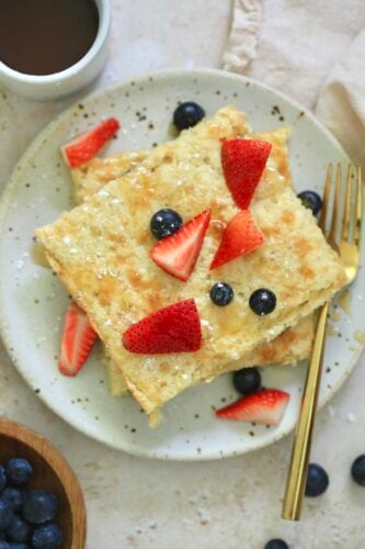 plate with square shaped pancakes and fruit on top.