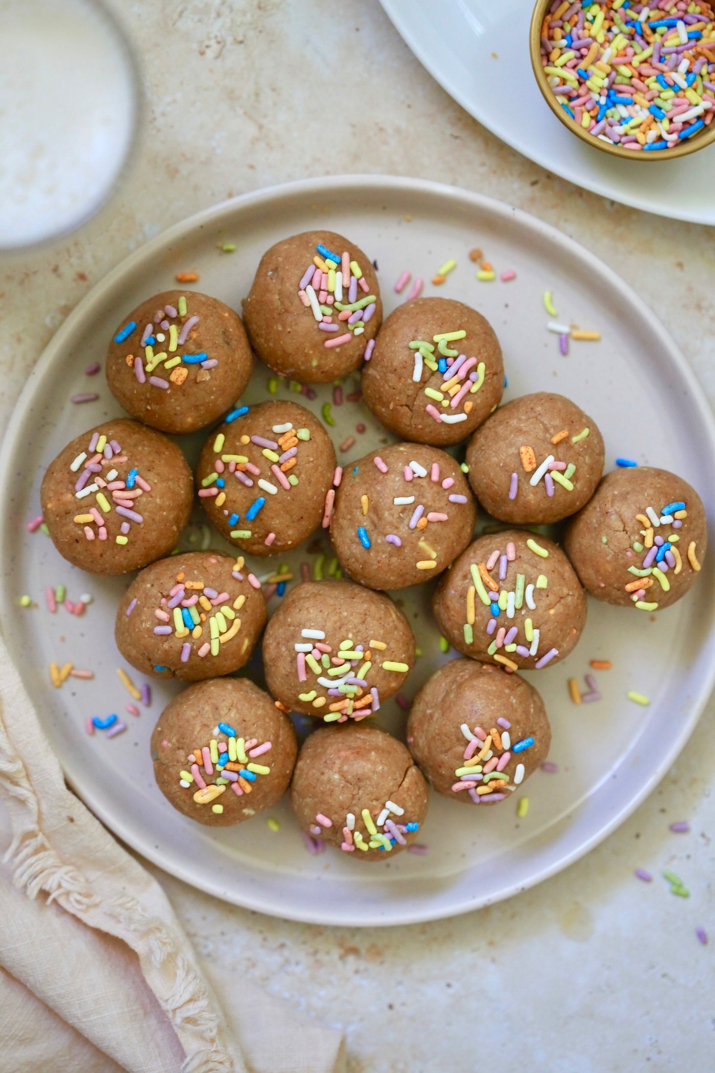 brown balls on plate with sprinkles and milk in background.