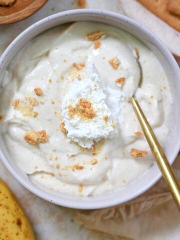bowl of white pudding with whipped cream and graham crumbs and gold spoon