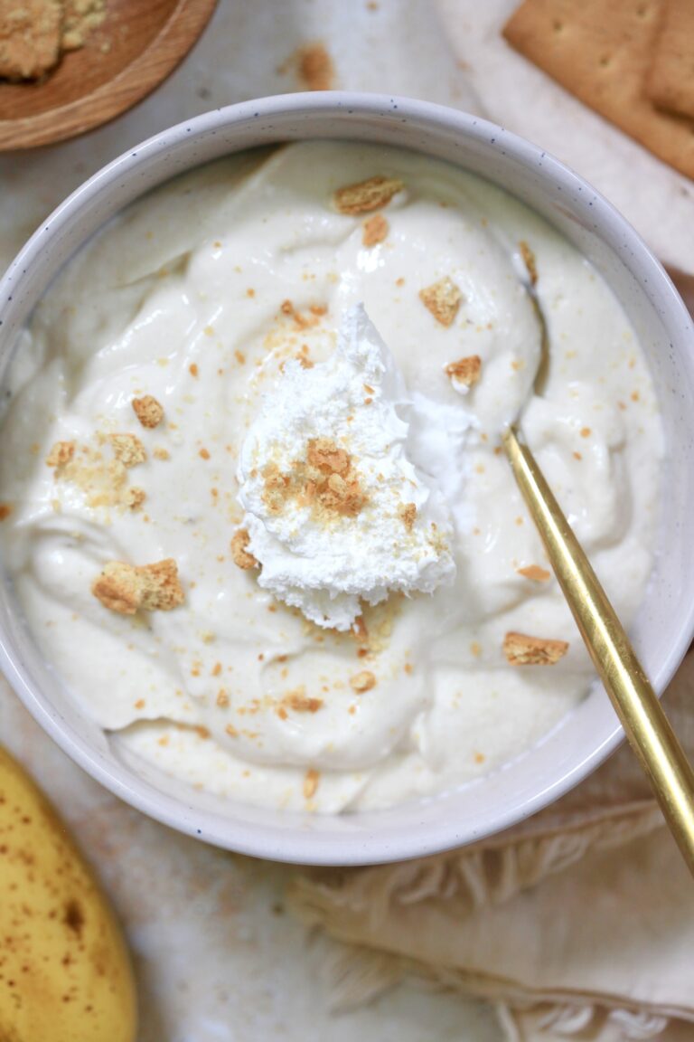bowl of white pudding with whipped cream and graham crumbs and gold spoon