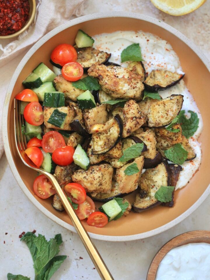 brown bowl with tofu, eggplant, tomato, and white sauce