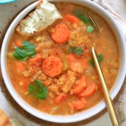 orange bowl of soup with carrots and gold spoon