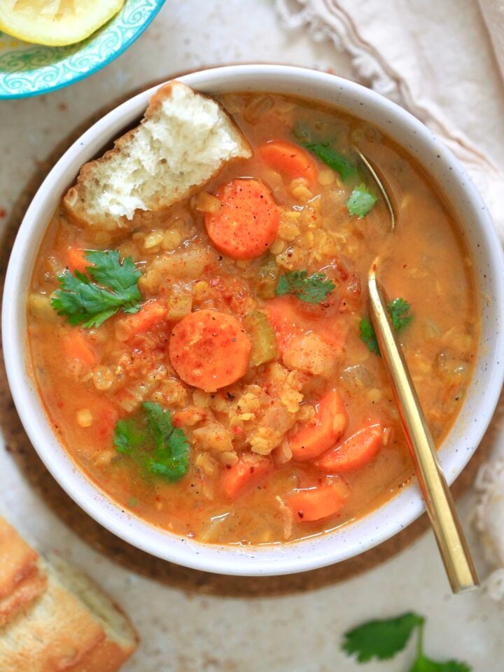 orange bowl of soup with carrots and gold spoon
