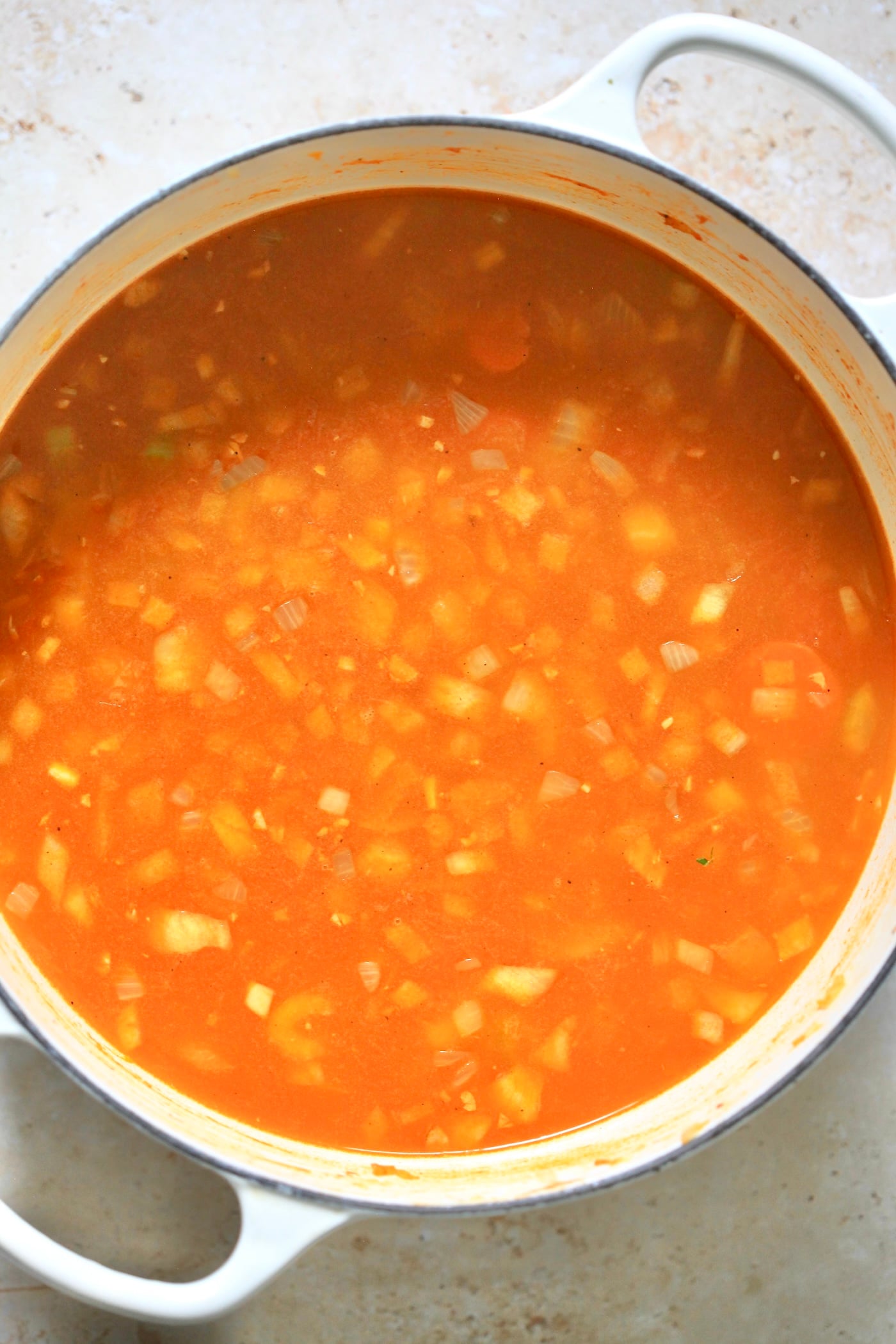 red broth with onions in white pot.