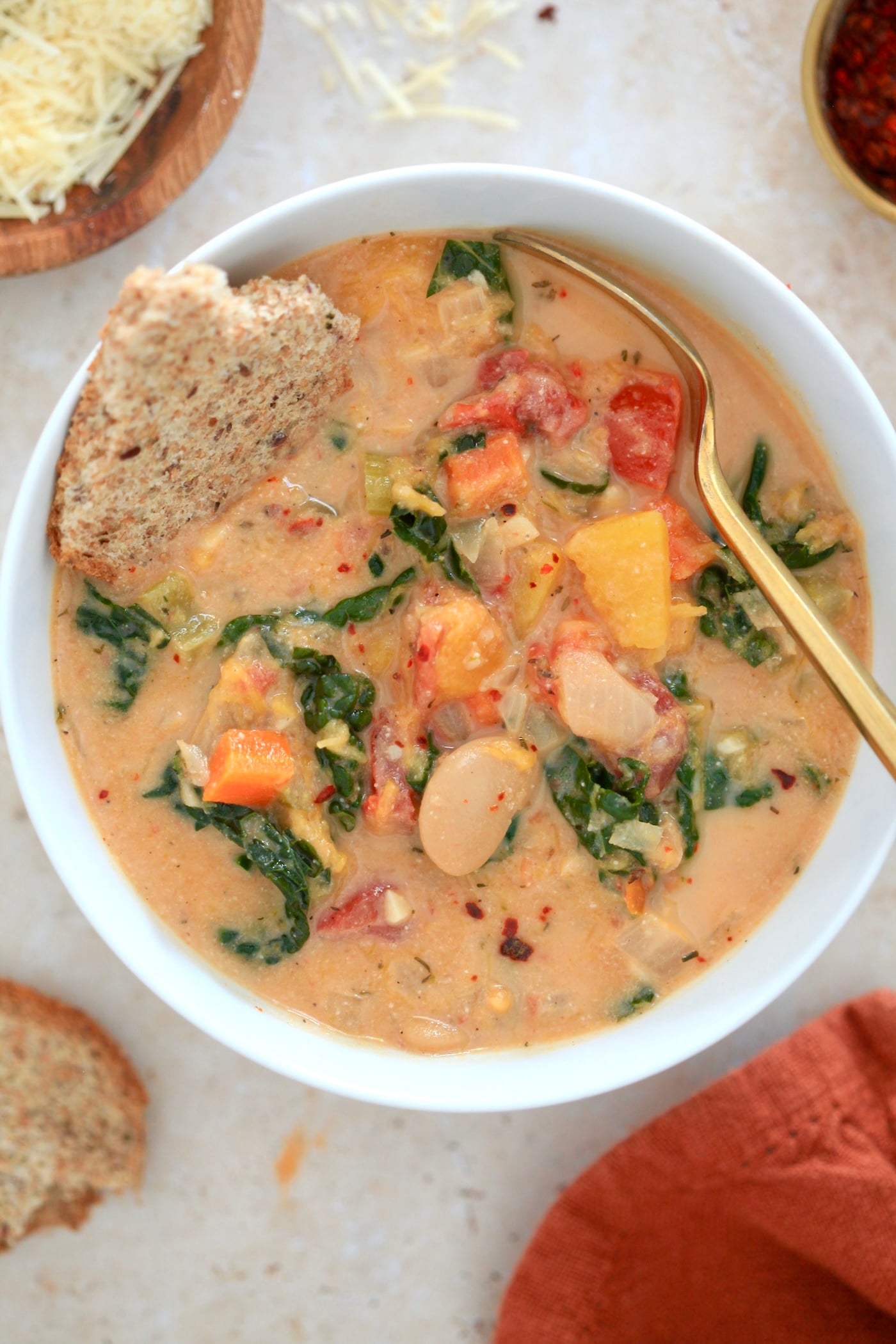 white bowl of tomato soup with kale and beans