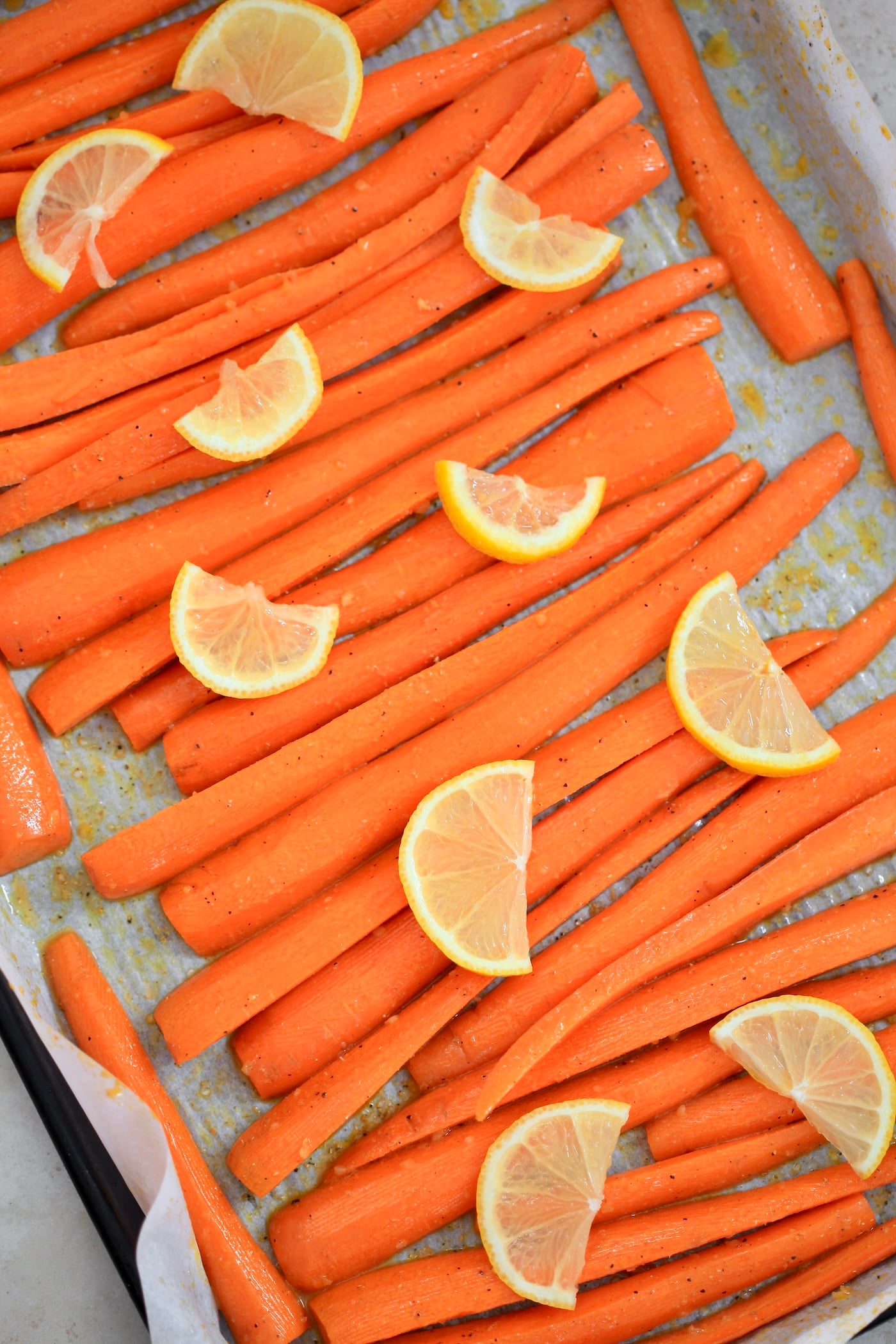 raw big carrots on baking sheet with lemons.