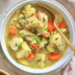 white bowl of chicken veggie soup with gold spoon.