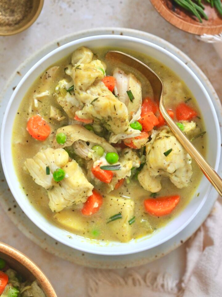 white bowl of chicken veggie soup with gold spoon.