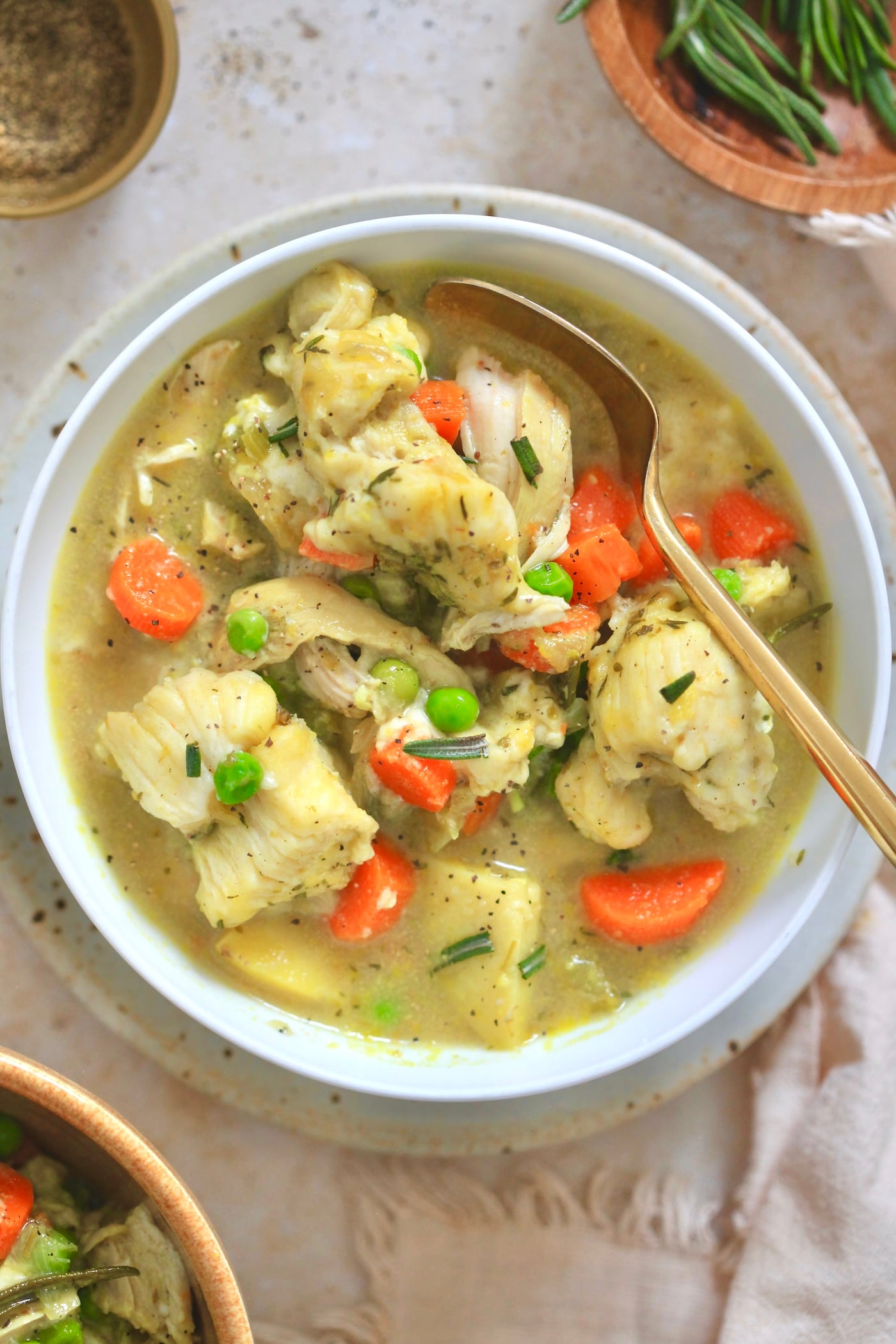 white bowl of chicken veggie soup with gold spoon.