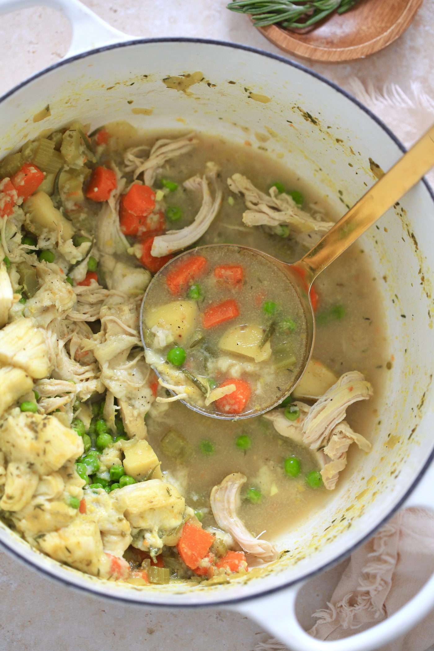 cooked chicken veggie soup in white pot with gold ladle.