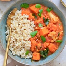 orange veggie mixture with brown rice in bowl with spoon.