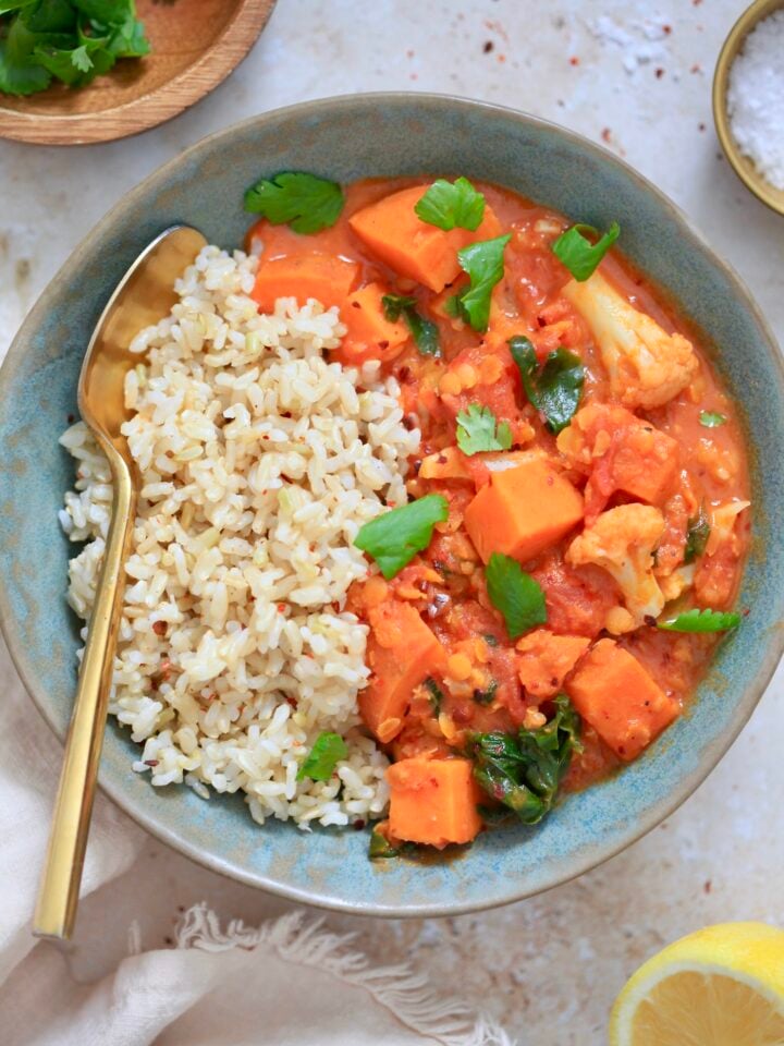 orange veggie mixture with brown rice in bowl with spoon.