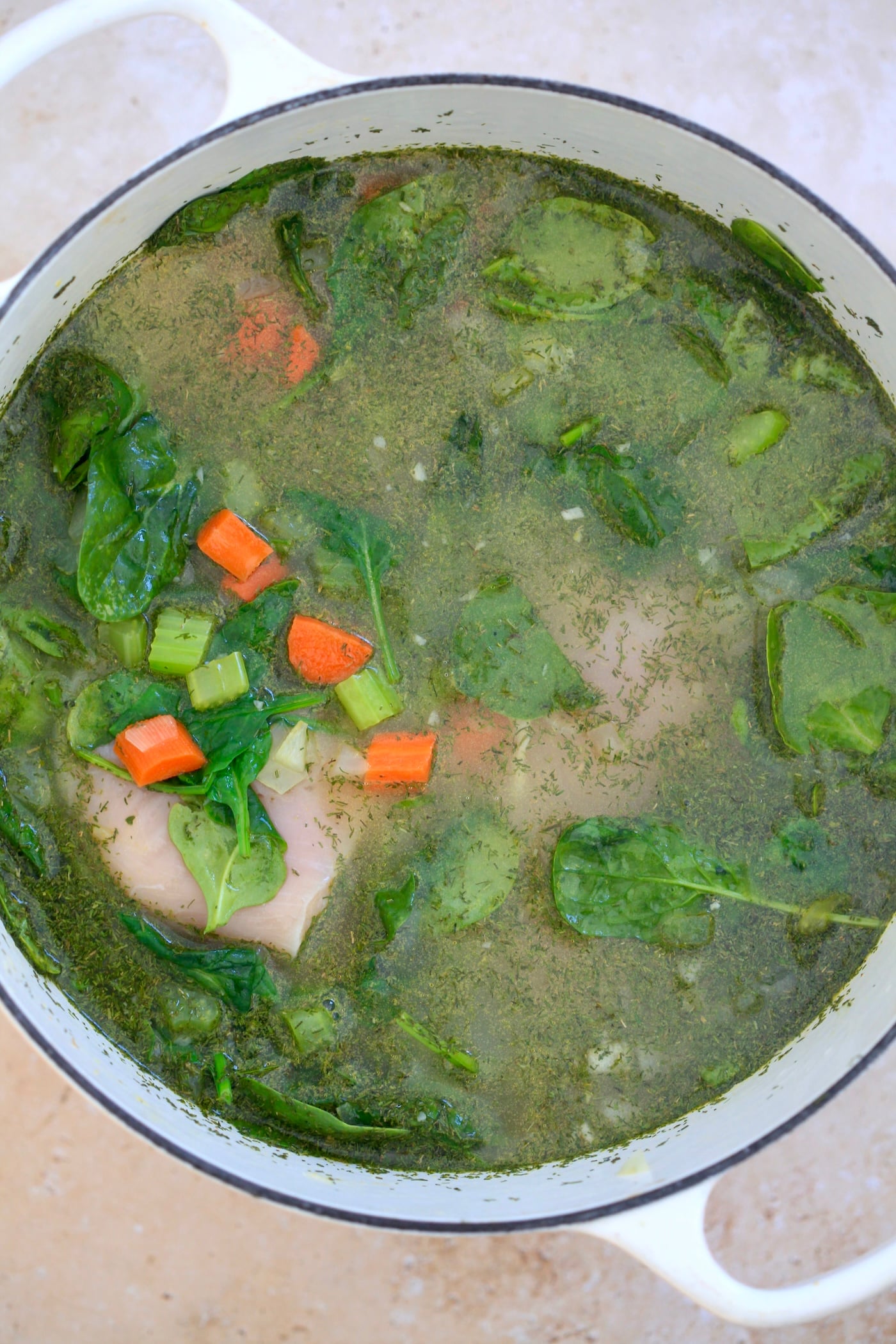 broth, veggies and raw chicken in pot.