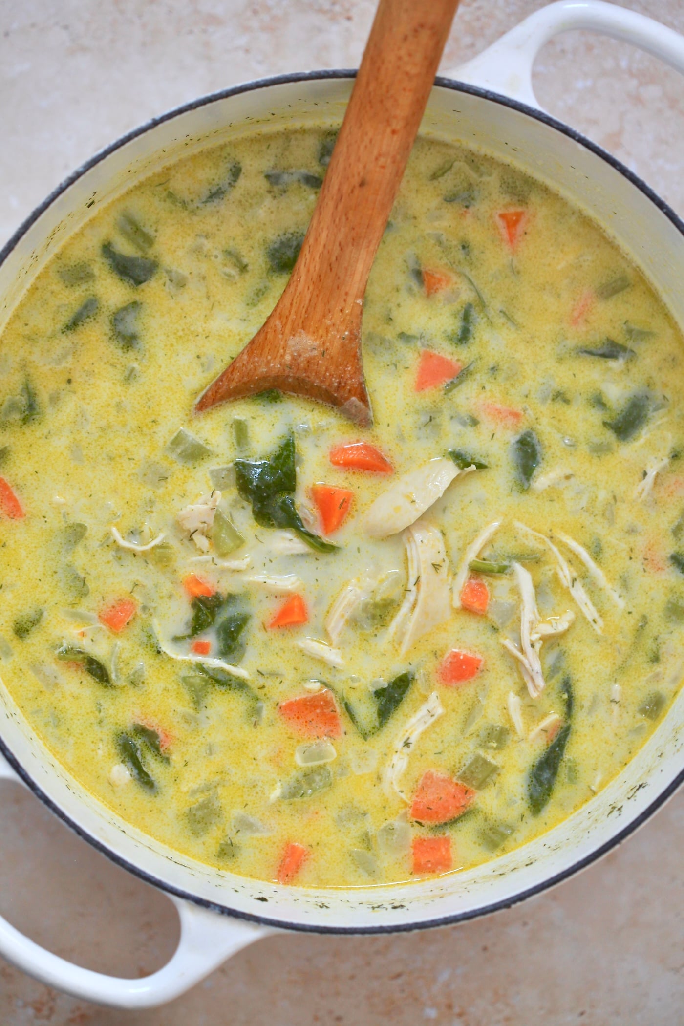 creamy yellow soup in pot with wooden spoon.