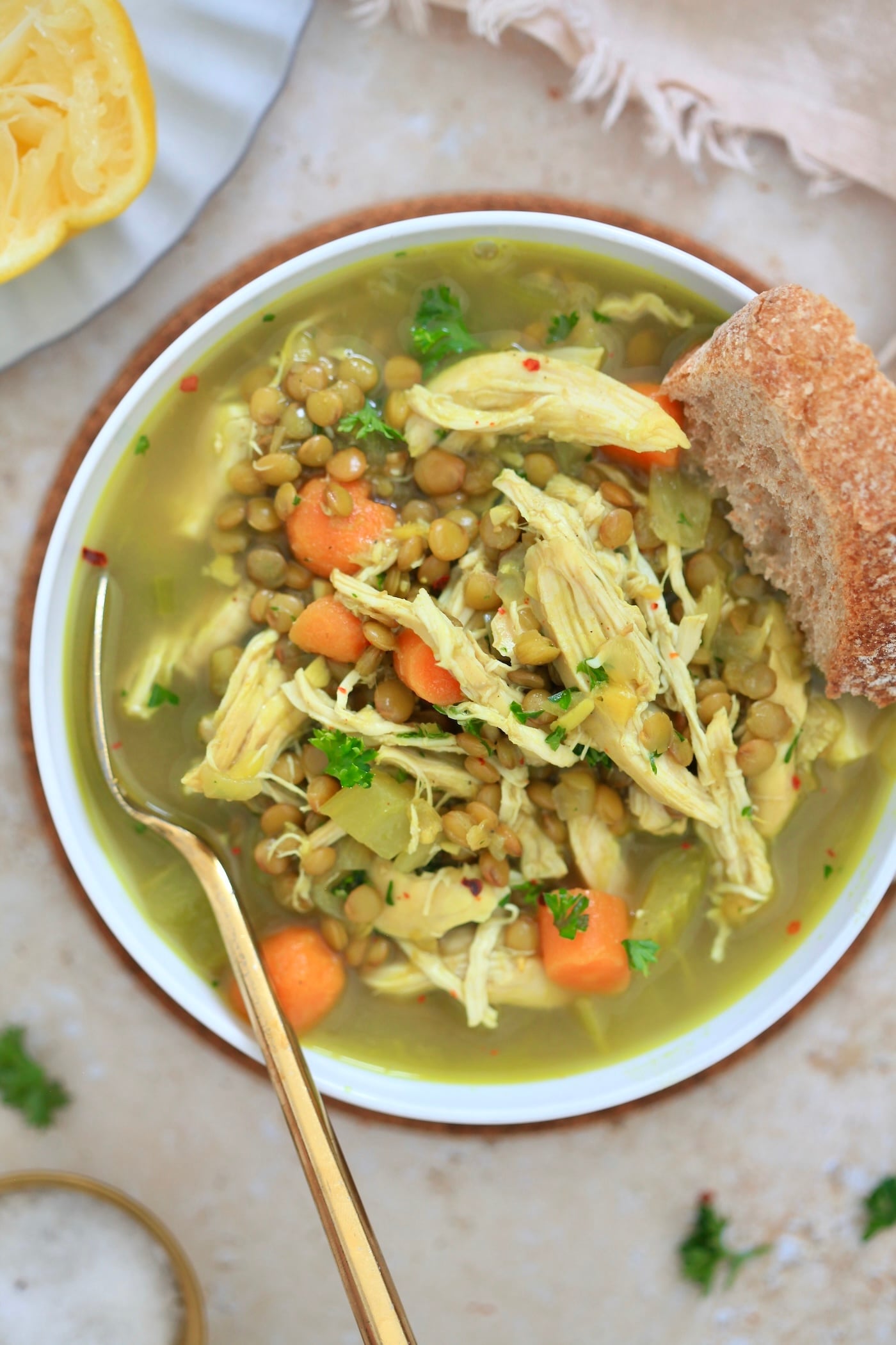 white bowl of golden soup with lentils and chicken and gold spoon