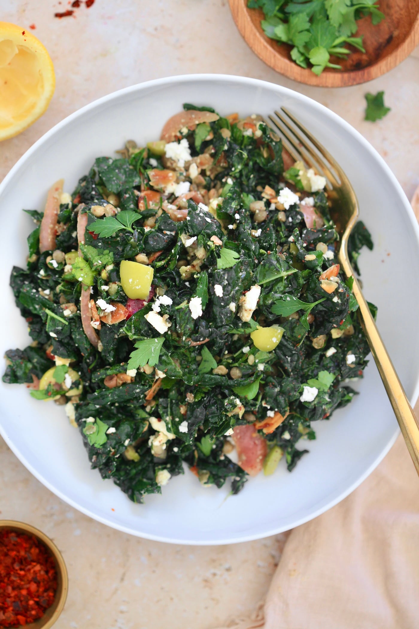 kale salad in white bowl with lemon and parsley in background.