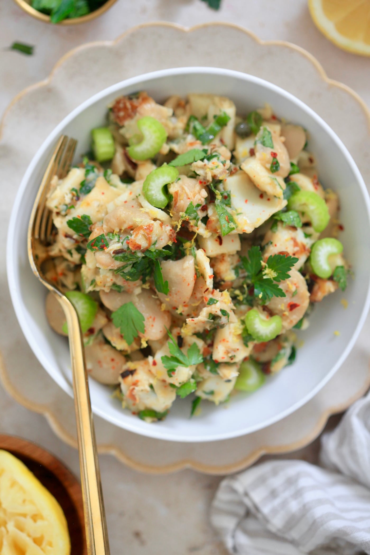 bowl with bean salad and celery with gold fork, lemons in background