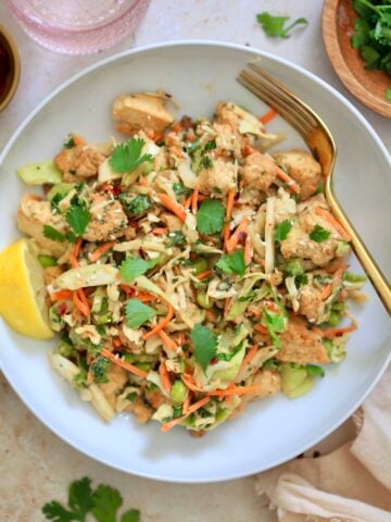 colorful cabbage salad in white bowl with gold fork.