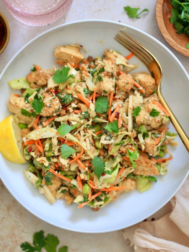 colorful cabbage salad in white bowl with gold fork.